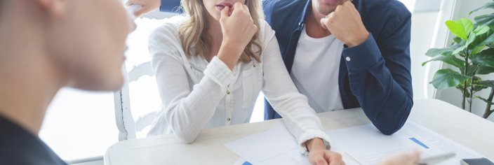 Real estate agent and worried couple look through documents.
