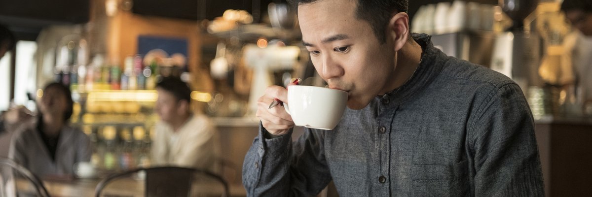 A young businessperson does paperwork in coffee shop and checks their phone.