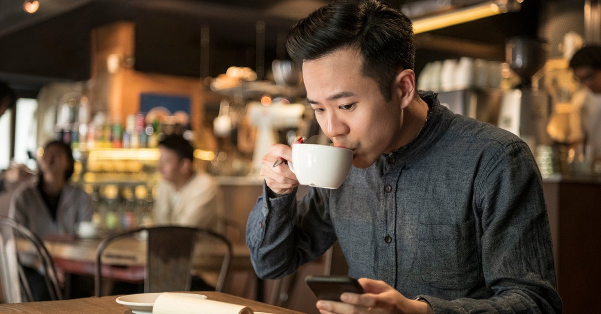 A young businessperson does paperwork in coffee shop and checks their phone.