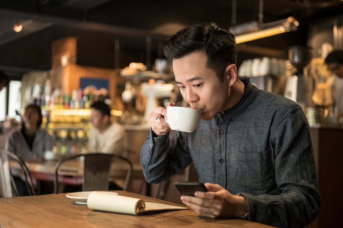 A young businessperson does paperwork in coffee shop and checks their phone.