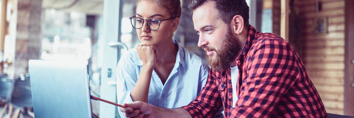 Two people in a casual public space discuss financial documents on a laptop and notepad.