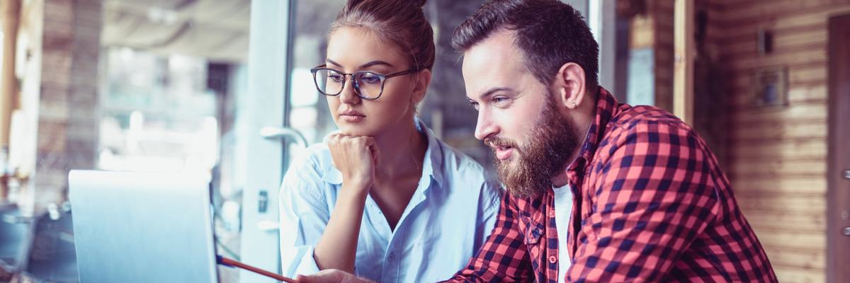 Two people in a casual public space discuss financial documents on a laptop and notepad.