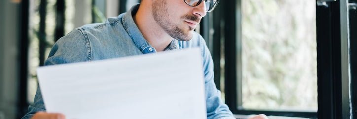 Man at desk holding document in one hand and typing with the other.