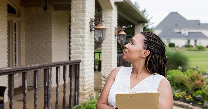 Woman stands outside house with a clipboard