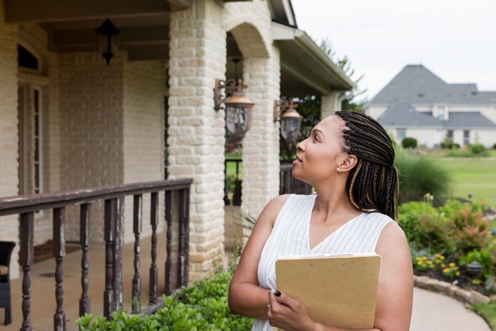 Woman stands outside house with a clipboard