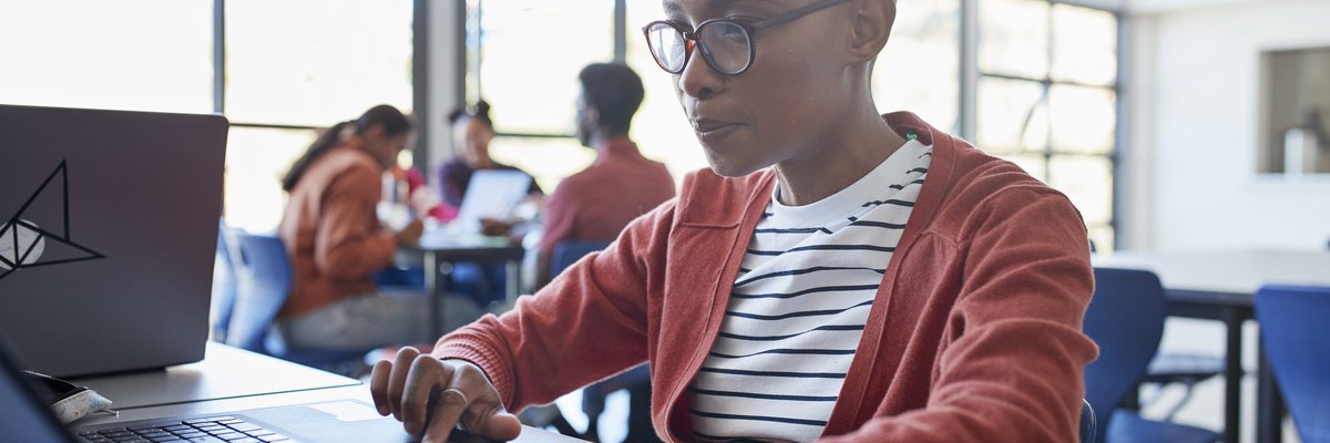 A bald student uses a laptop while sitting in a university classroom.