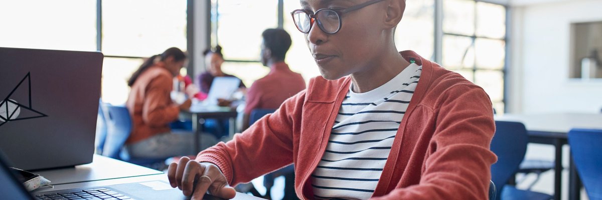 A bald student uses a laptop while sitting in a university classroom.