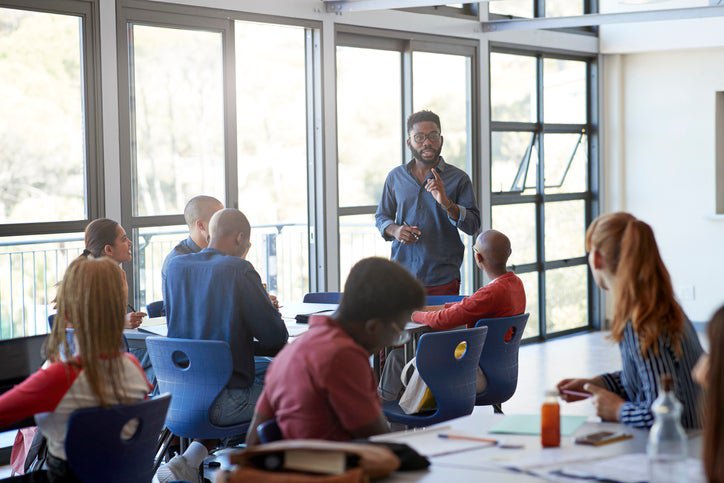 A teacher lectures in front of a group of teenagers in a classroom.