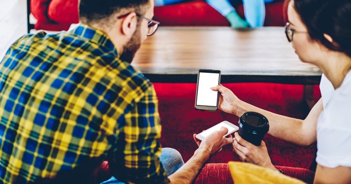 Two people show each other their phones while drinking coffee.