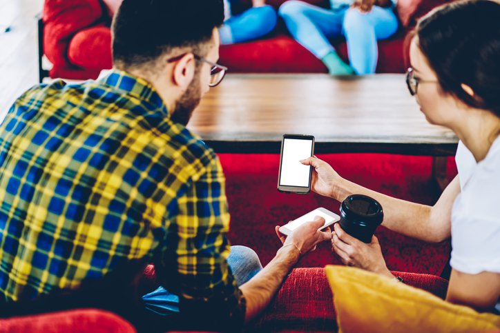 Two people show each other their phones while drinking coffee.