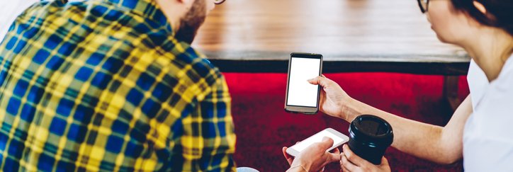 Two people show each other their phones while drinking coffee.