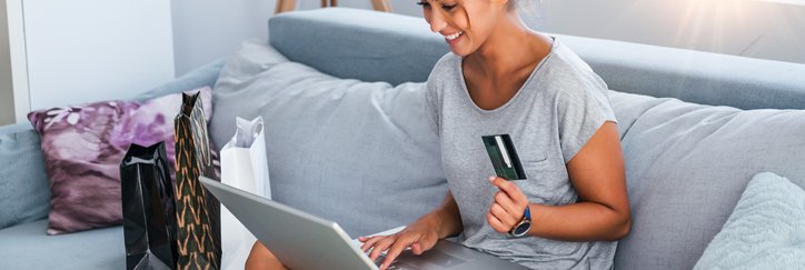 Smiling woman with laptop sits cross legged on sofa holding a credit card.