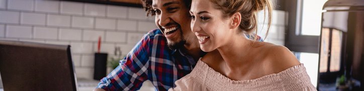 Happy couple reviewing their bank accounts on a laptop and on paper at a desk