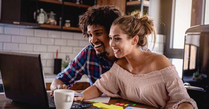 Happy couple reviewing their bank accounts on a laptop and on paper at a desk