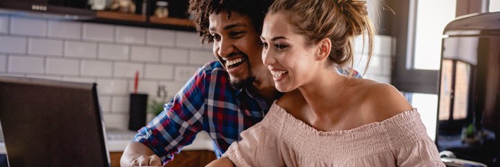 Happy couple reviewing their bank accounts on a laptop and on paper at a desk