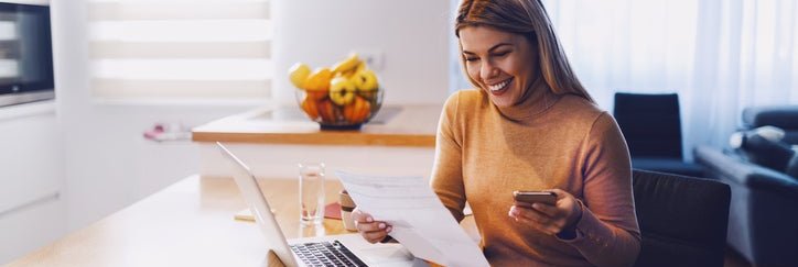 Happy woman reviewing paperwork and a laptop at home
