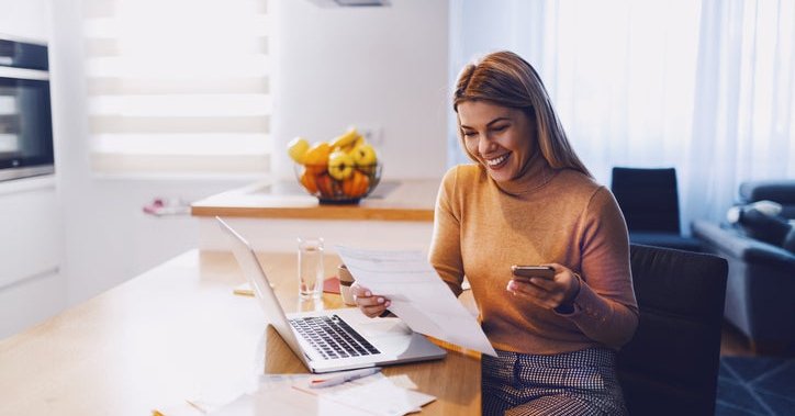 Happy woman reviewing paperwork and a laptop at home