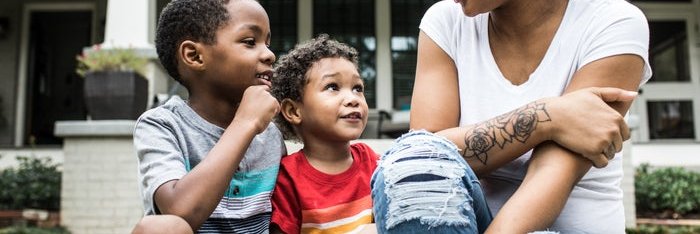 A mother talking with her two young sons while sitting in front of a house