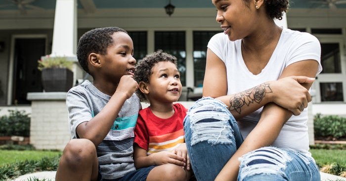 A mother talking with her two young sons while sitting in front of a house