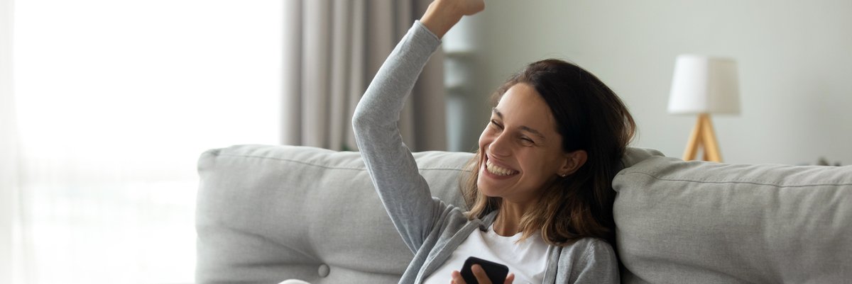 Person sitting on couch pumps fist in celebration while holding cellphone.