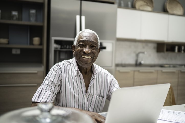 Man with broad smile on his face sits in front of computer.