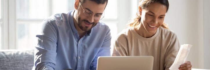 Happy couple sit in front of computer with paperwork .