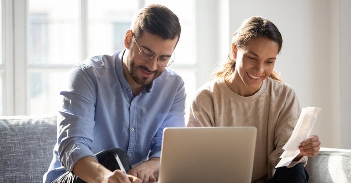 Happy couple sit in front of computer with paperwork .