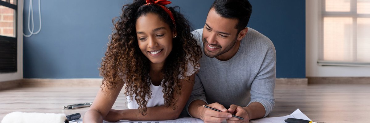 A couple looks at the blueprints of their new house while lying on the floor smiling.