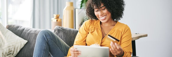 Young African American woman uses her tablet and credit card to shop online from home.