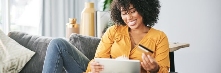 Young African American woman uses her tablet and credit card to shop online from home.