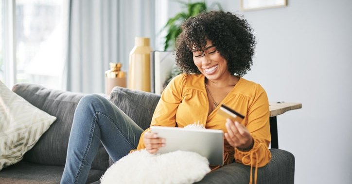 Young African American woman uses her tablet and credit card to shop online from home.