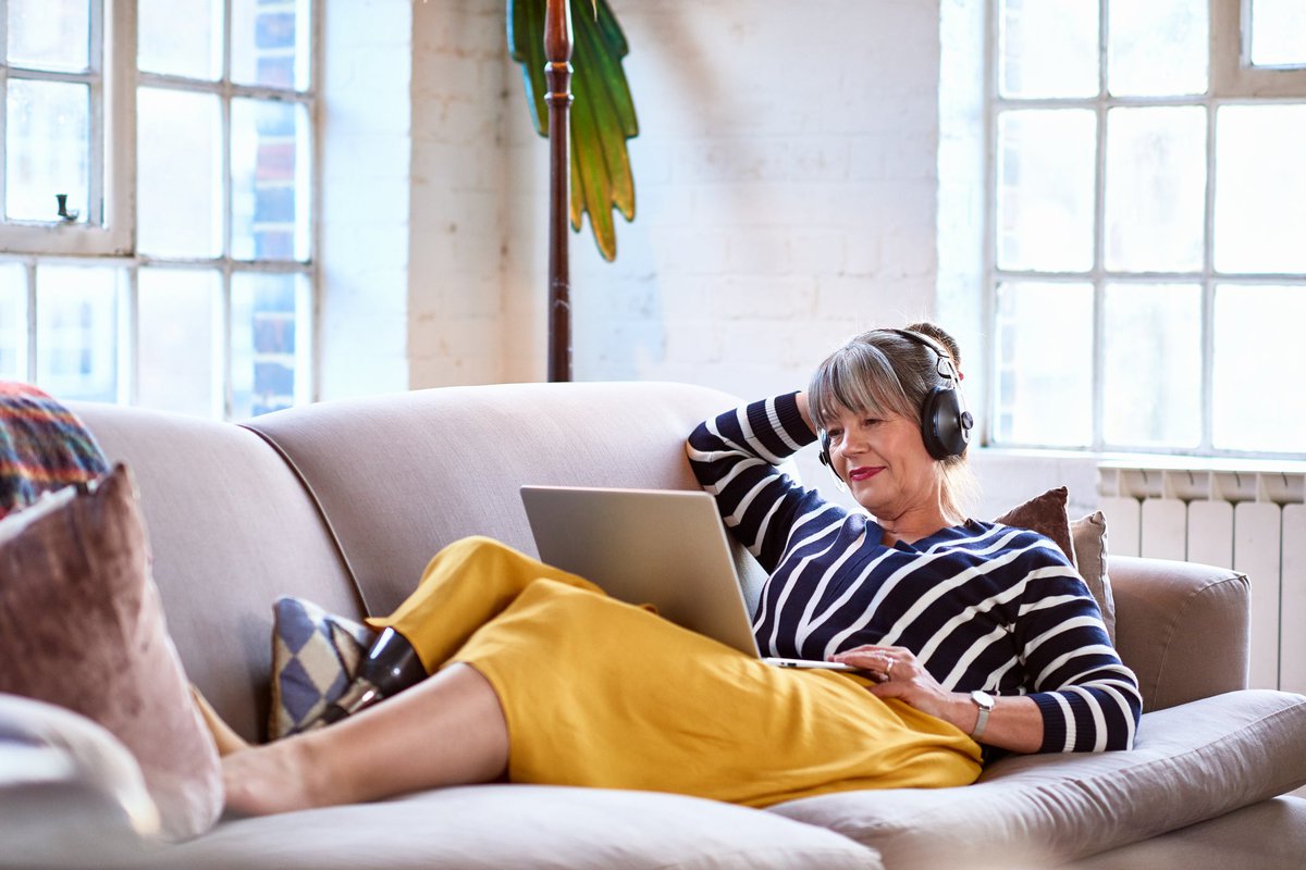 A person wearing headphones looks a their computer while lounging on the couch.