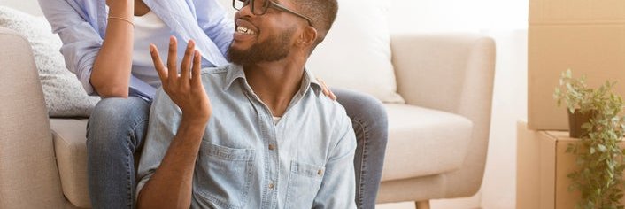 A couple sits in their living room, smiling as they look at a laptop.