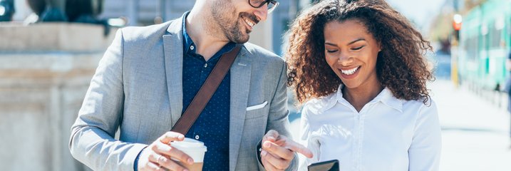 Two happy friends look at something on a phone outside in the city during the day