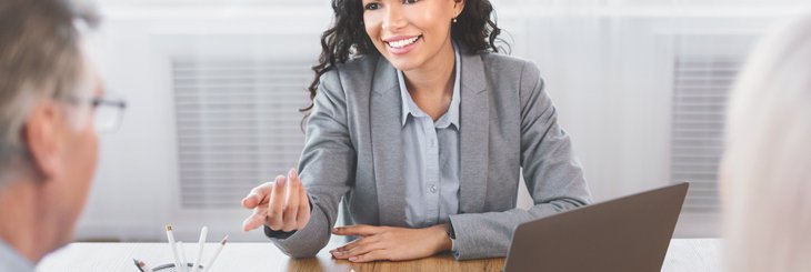 Smiling woman gestures to gray-haired man over desk.