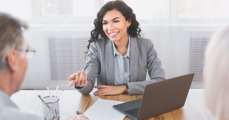 Smiling woman gestures to gray-haired man over desk.