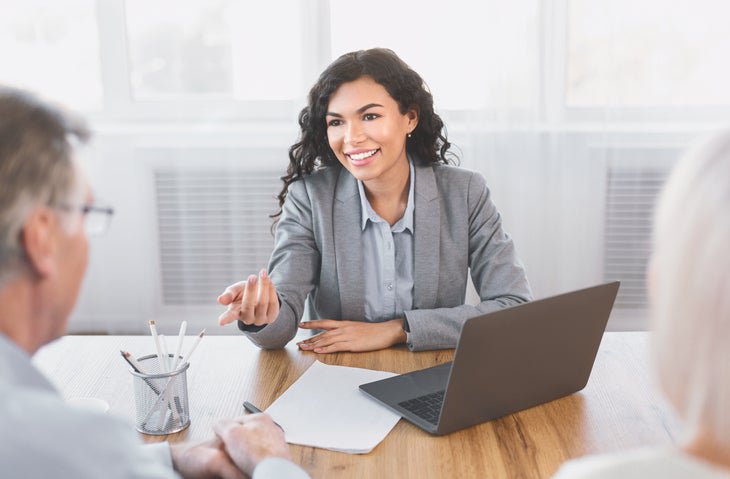 Smiling woman gestures to gray-haired man over desk.