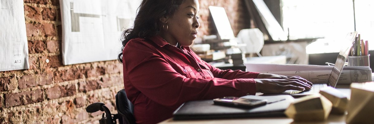A business professional uses a laptop and wheelchair at a desk in an office.