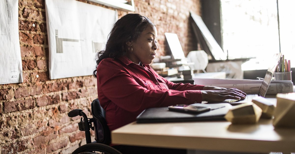 A business professional uses a laptop and wheelchair at a desk in an office.
