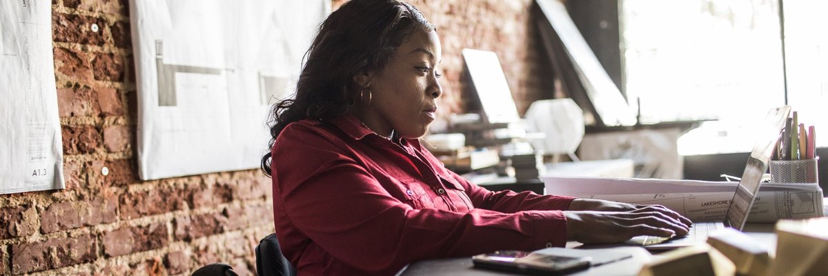 A business professional uses a laptop and wheelchair at a desk in an office.