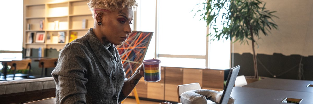A professional uses a laptop and holds a rainbow coffee mug in a coworking space.