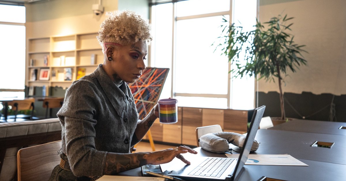A professional uses a laptop and holds a rainbow coffee mug in a coworking space.