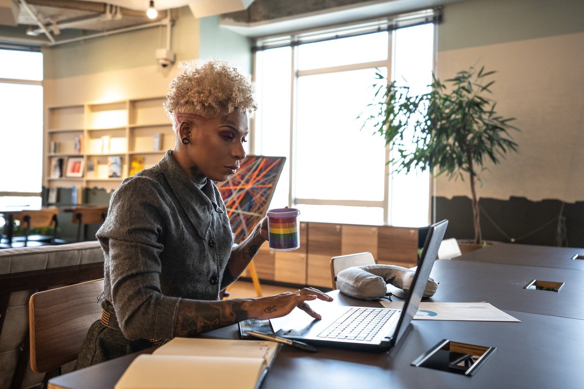 Un Professionnel Utilise Un Ordinateur Portable Et Tient Une Tasse À Café Arc-En-Ciel Dans Un Espace De Coworking.