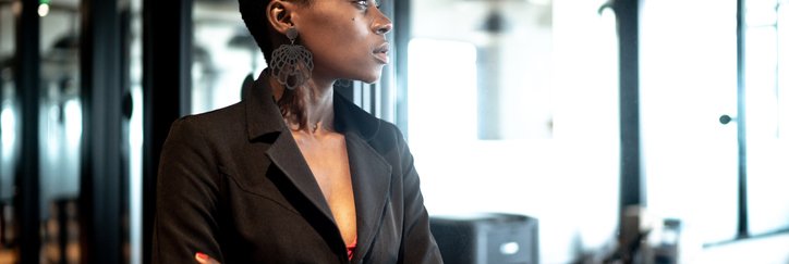 Young woman looks into distance with office in background.