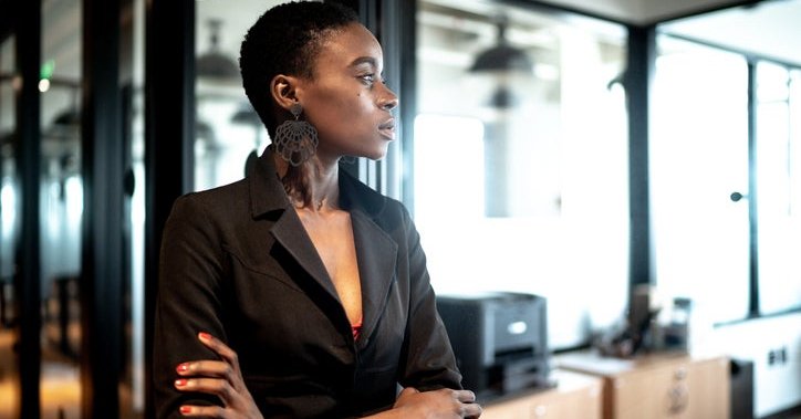 Young woman looks into distance with office in background.