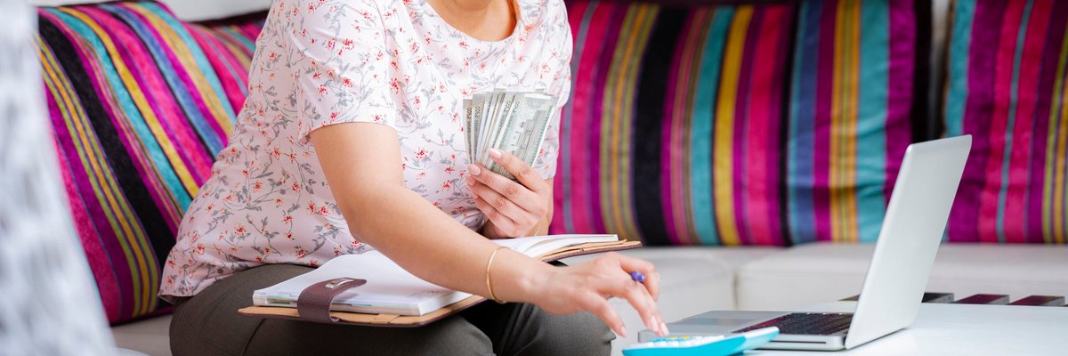Woman sitting on sofa holding cash and using a calculator.