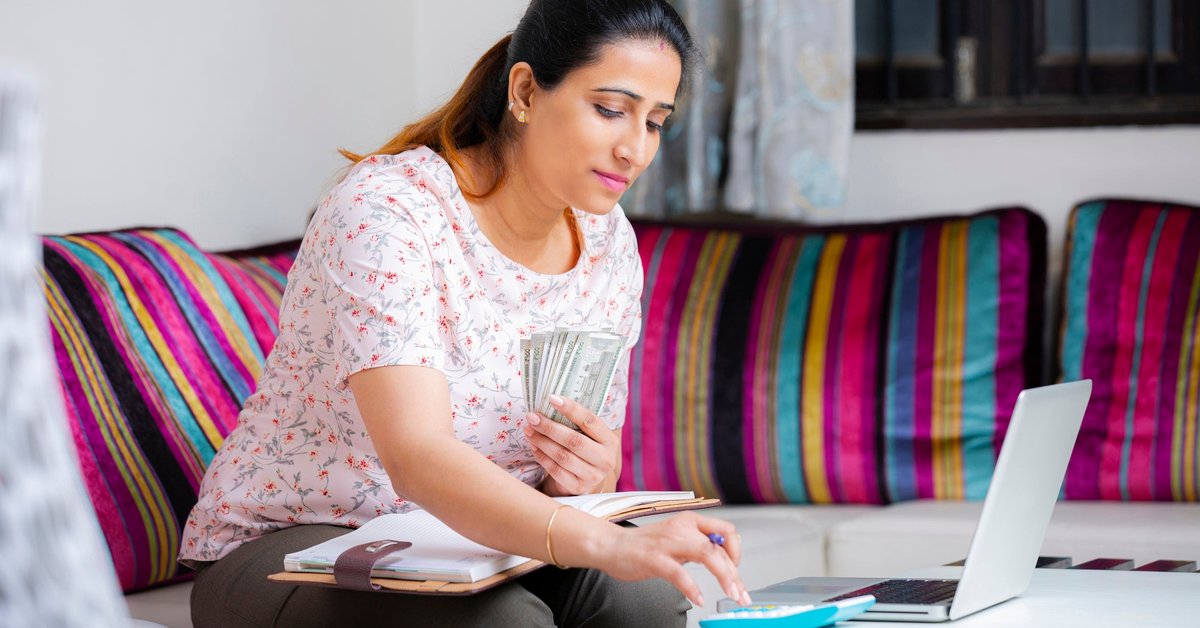 Woman sitting on sofa holding cash and using a calculator.