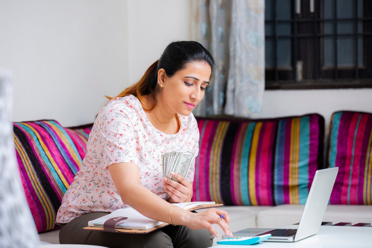 Woman sitting on sofa holding cash and using calculator.