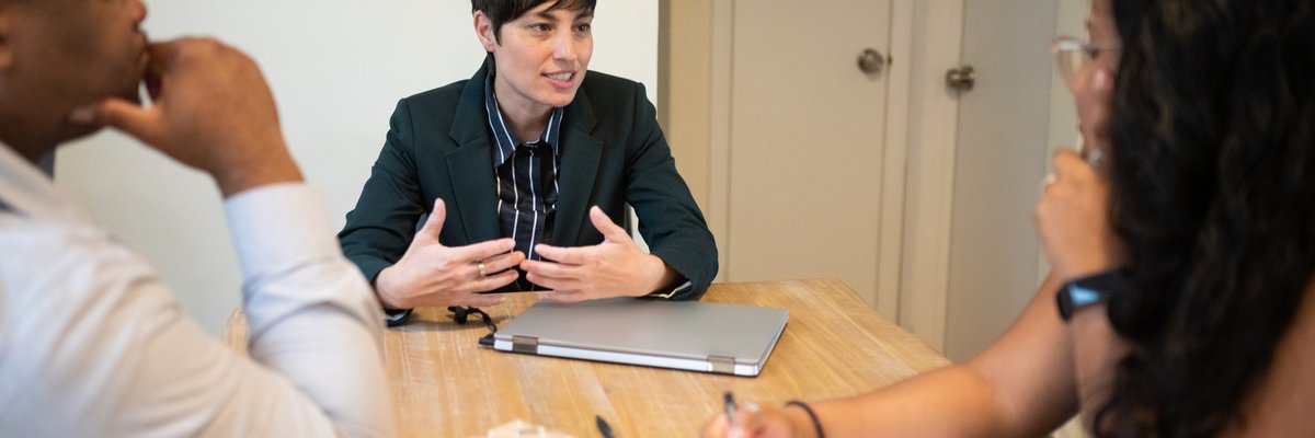 One businessperson leads an office meeting with two other workers.