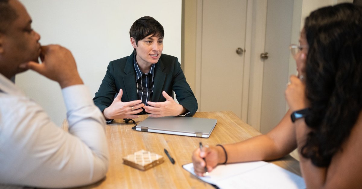 One businessperson leads an office meeting with two other workers.